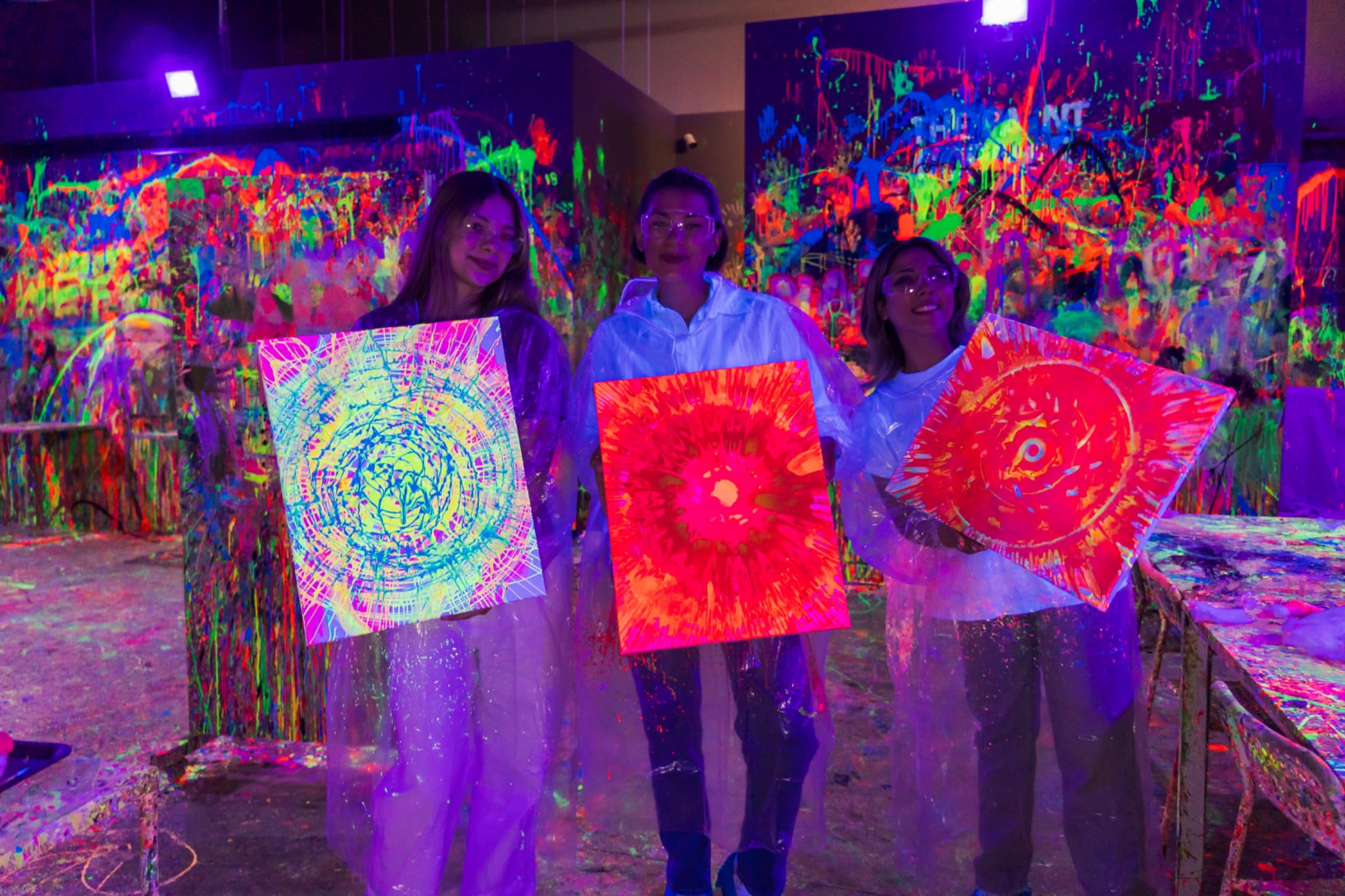 Three women holding their neon spin-art canvases at Ladies Night, The Paint Corner Murouj
